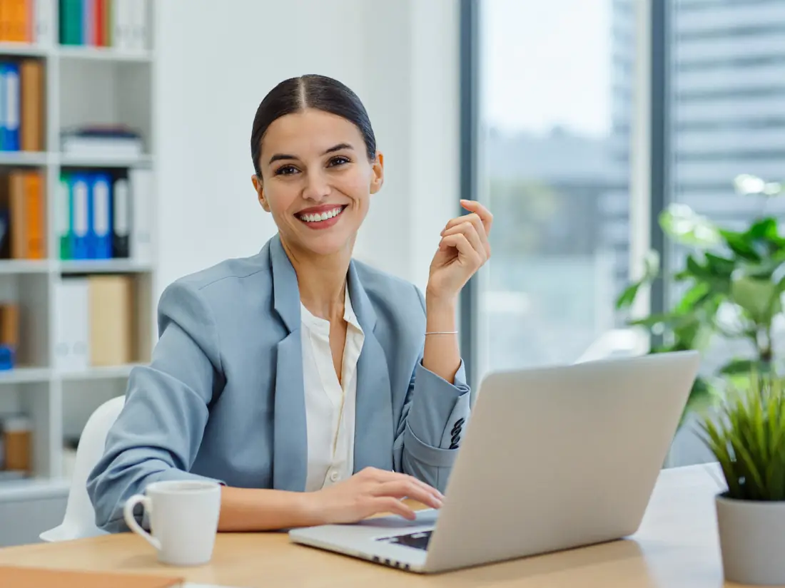 A friendly tax professional smiling while working at a laptop in a bright office.